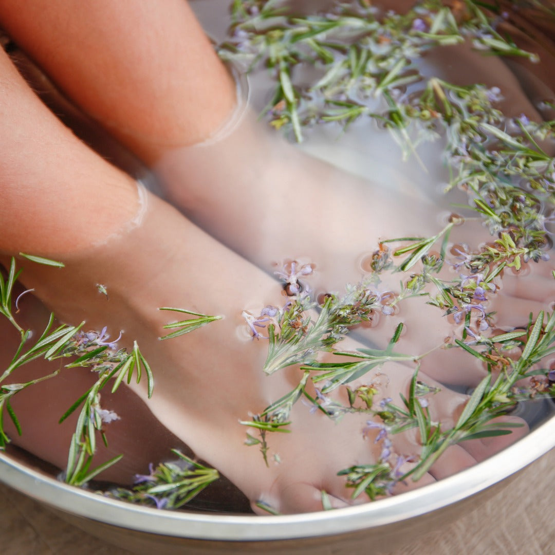 Child's feet in a bowl of water with lavender and rosemary, suggesting a relaxing foot soak.