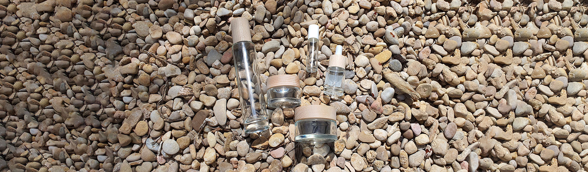 Recycled glass containers with wooden lit laying on small smooth rocks